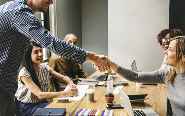 Junge Menschen interagieren freundlich rund um einen Tisch, teils sitzend, teils stehend.