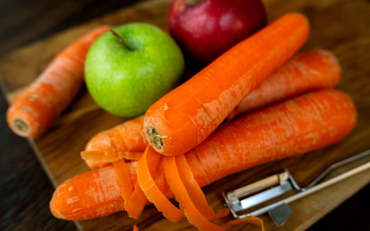 Auf dem Bild sind neben Karotten auch Äpfel auf einem Schneidebrett zu erkennen.