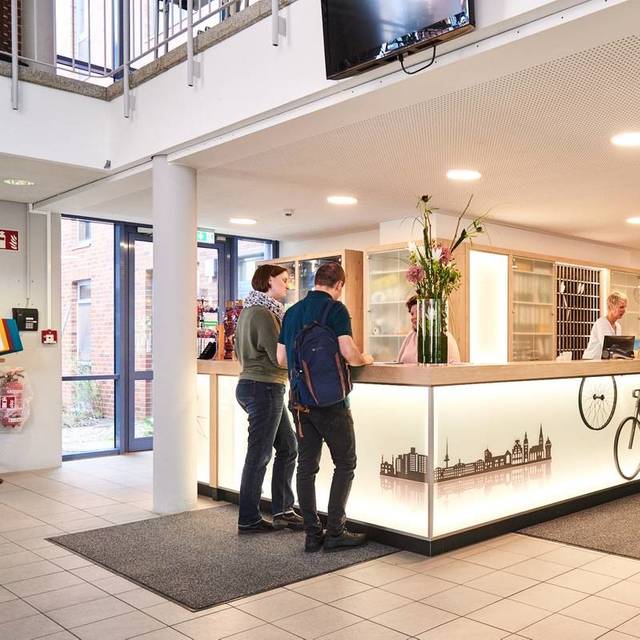 Der Empfangsbereich des Jugendgästehauses am Aasee in Münster. An einer Theke stehen Menschen.