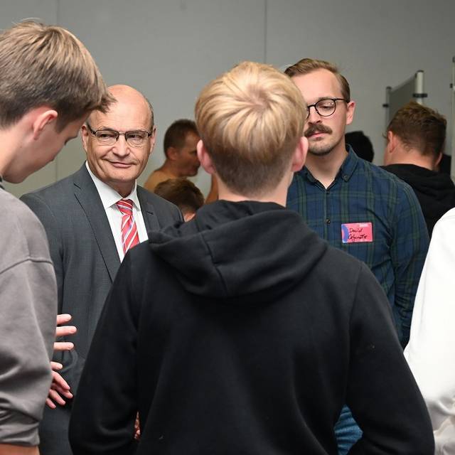 Menschengruppe im Gespräch: Zwei Jugendliche von hinten. Im Zentrum lächelt der Landrat.