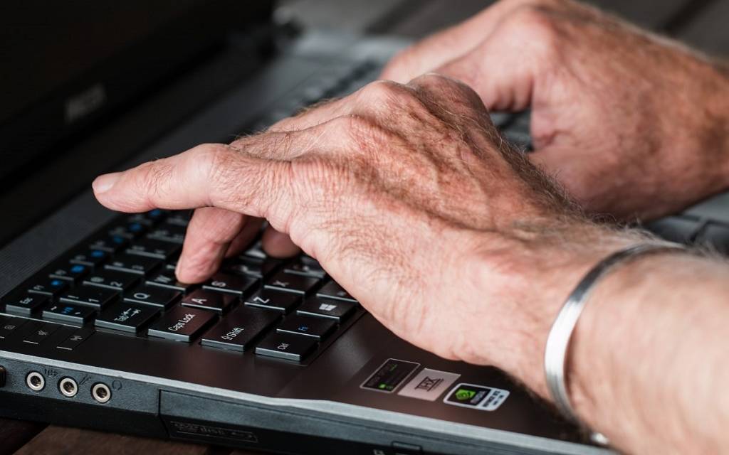 Männer-Hände, die auf einer Tastatur tippen. Links ein silberner Armreif.