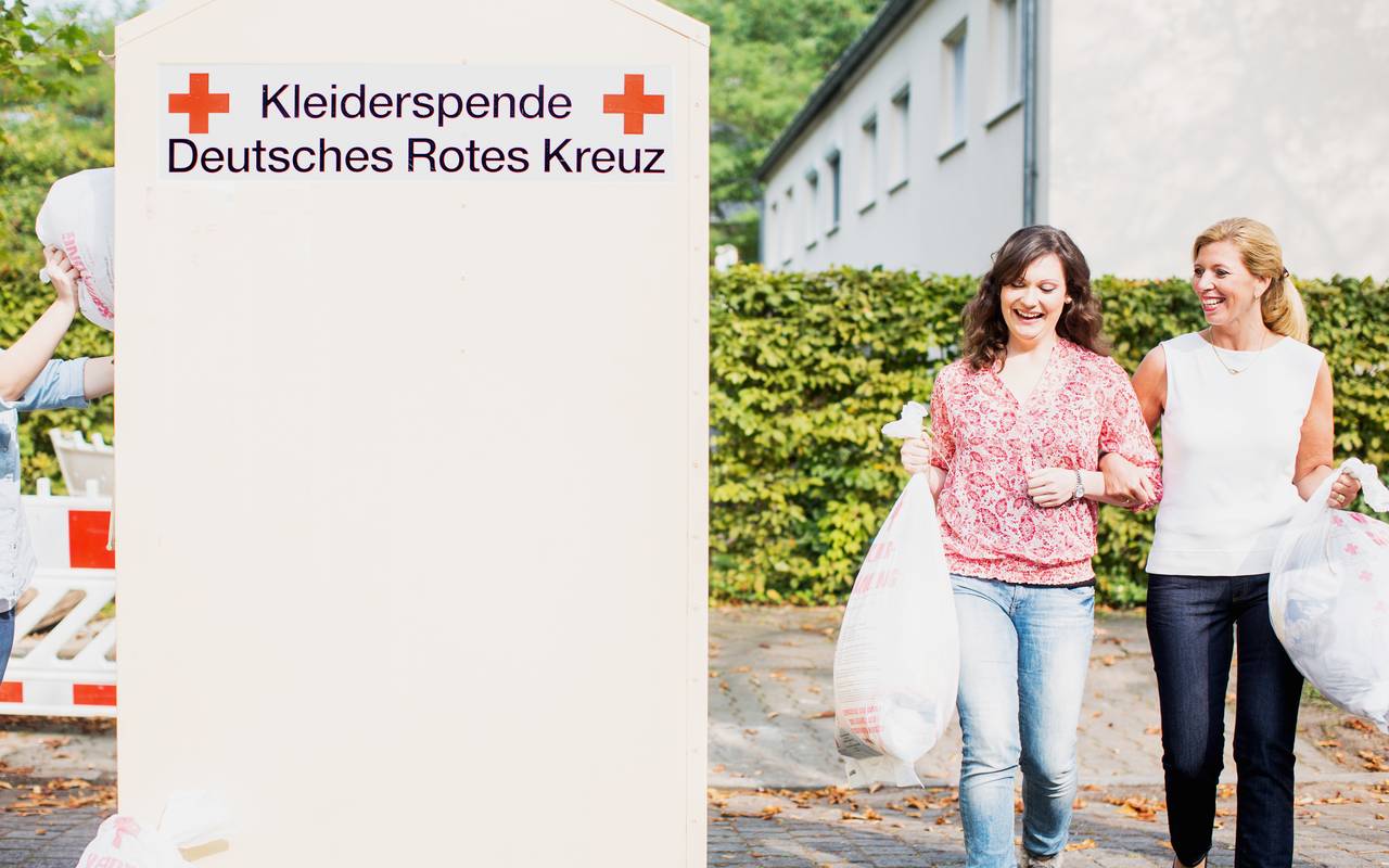 Zwei Frauen gehen zu einem Altkleidercontainer des Deutschen Roten Kreuzes