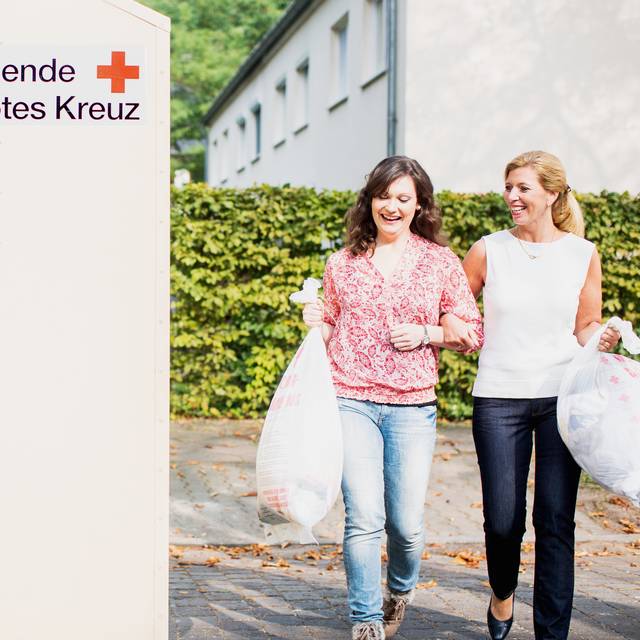 Zwei Frauen gehen zu einem Altkleidercontainer des Deutschen Roten Kreuzes