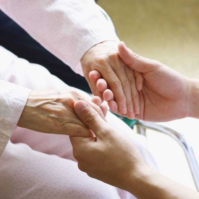 junge Hände eines Pflegers halten die Hände einer alten Dame