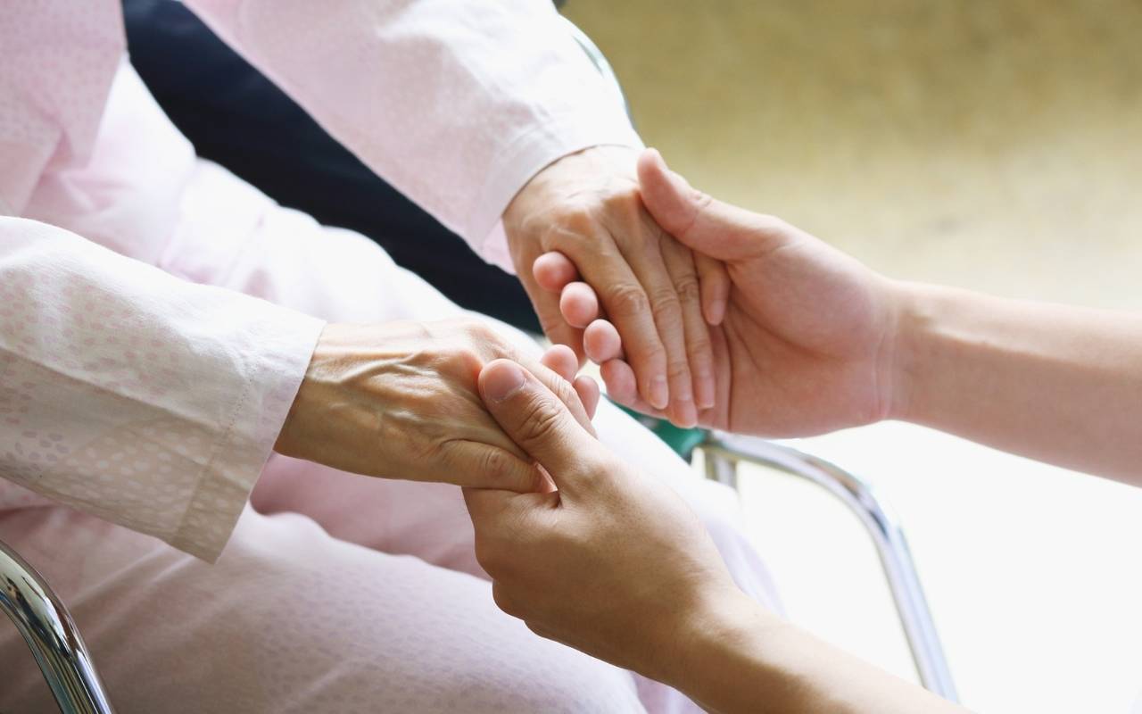 junge Hände eines Pflegers halten die Hände einer alten Dame