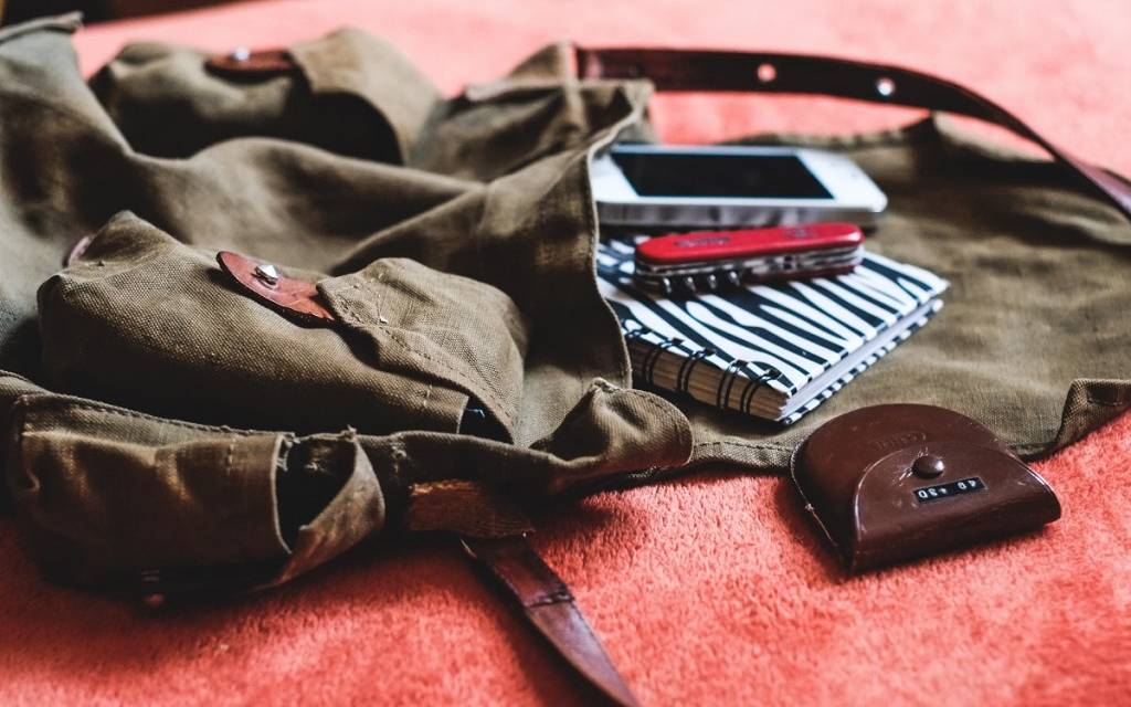 Ein leerer Retro-Rucksack, offen, auf einer hellroten Frottier-Decke. "Herausgerutscht": Handy, Taschenmesser, Schlüsseletui und Notizblock