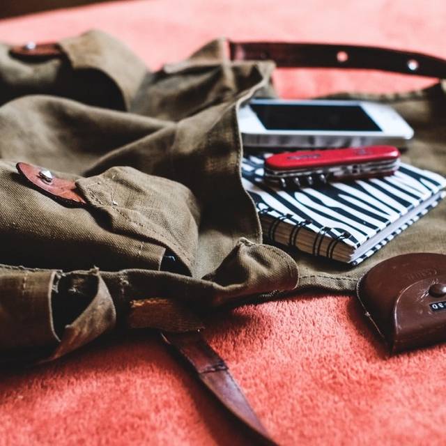 Ein leerer Retro-Rucksack, offen, auf einer hellroten Frottier-Decke. "Herausgerutscht": Handy, Taschenmesser, Schlüsseletui und Notizblock