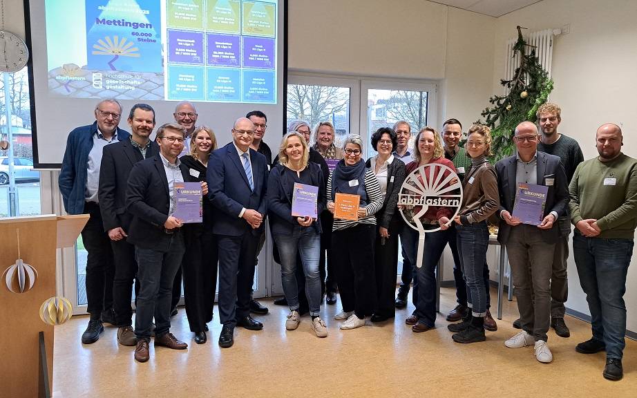 Gruppenbild aller Ausgezeichneten mit Preisen und Urkunden, darunter eine "Ewige Blume" aus Metall. Im Hintergrund ein Monitor mit Infos zum Mettinger Projekt.