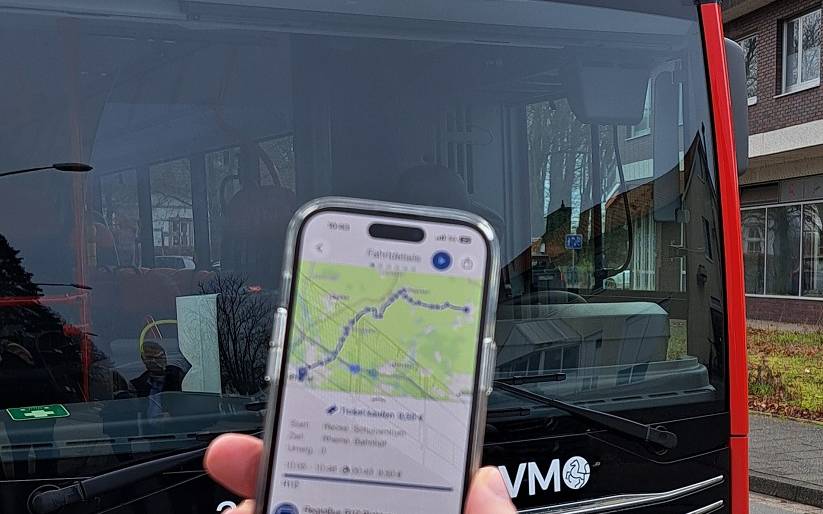 Im Hintergrund ein RVM-Bus, im Vordergrund eine Hand, die ein Handy hält. Darauf zu sehen: Die neue Busverbindung in der App.