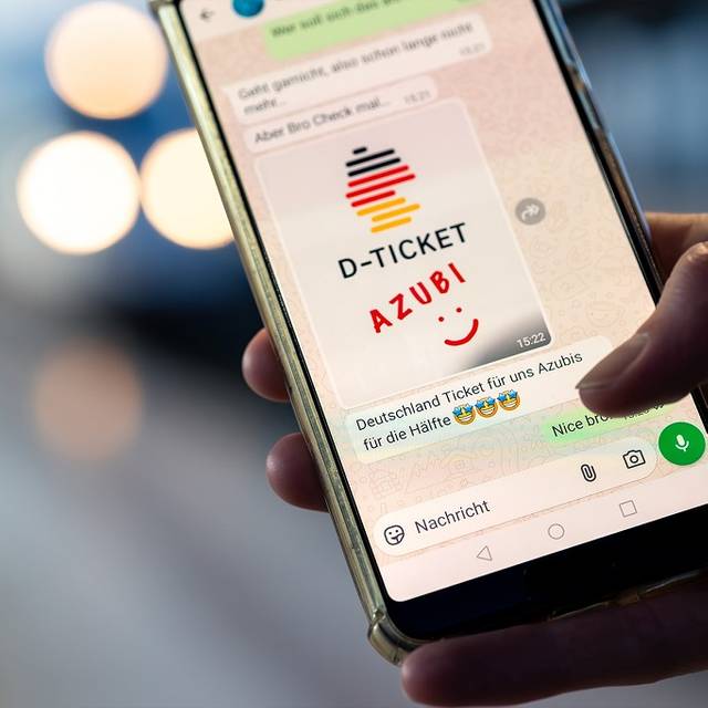 Ein Handy in einer Hand. Auf dem Bildschirm eine WhatsApp-Meldung mit Bild: D-Ticket AZUBI und ein Smiley. Darunter eine Nachricht: Deutschland Ticket für uns Azubis für die Hälfte. Und drei Strahle-Smileys