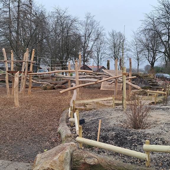 Eine entsiegelte Fläche mit frisch gepflanzten Bäumen, Sträuchern und Stauden. Dazwischen naturnahe Spielgeräte und eine Häcksel-Schicht