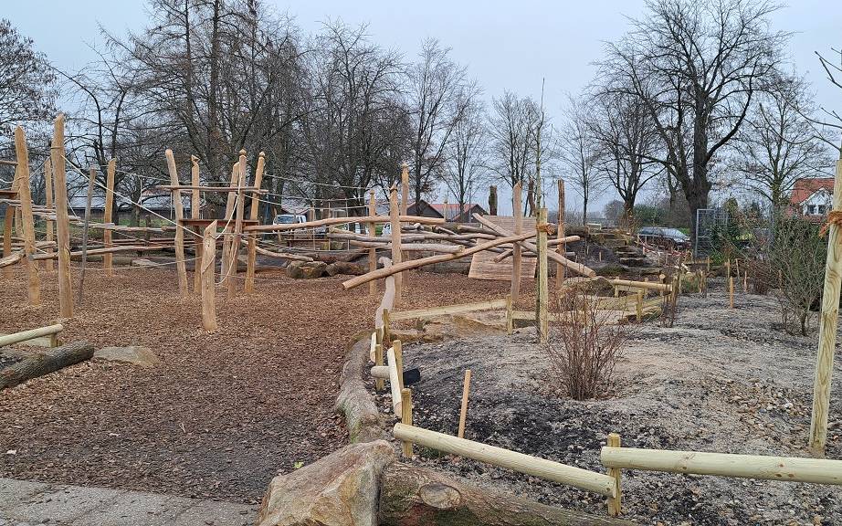 Eine entsiegelte Fläche mit frisch gepflanzten Bäumen, Sträuchern und Stauden. Dazwischen naturnahe Spielgeräte und eine Häcksel-Schicht