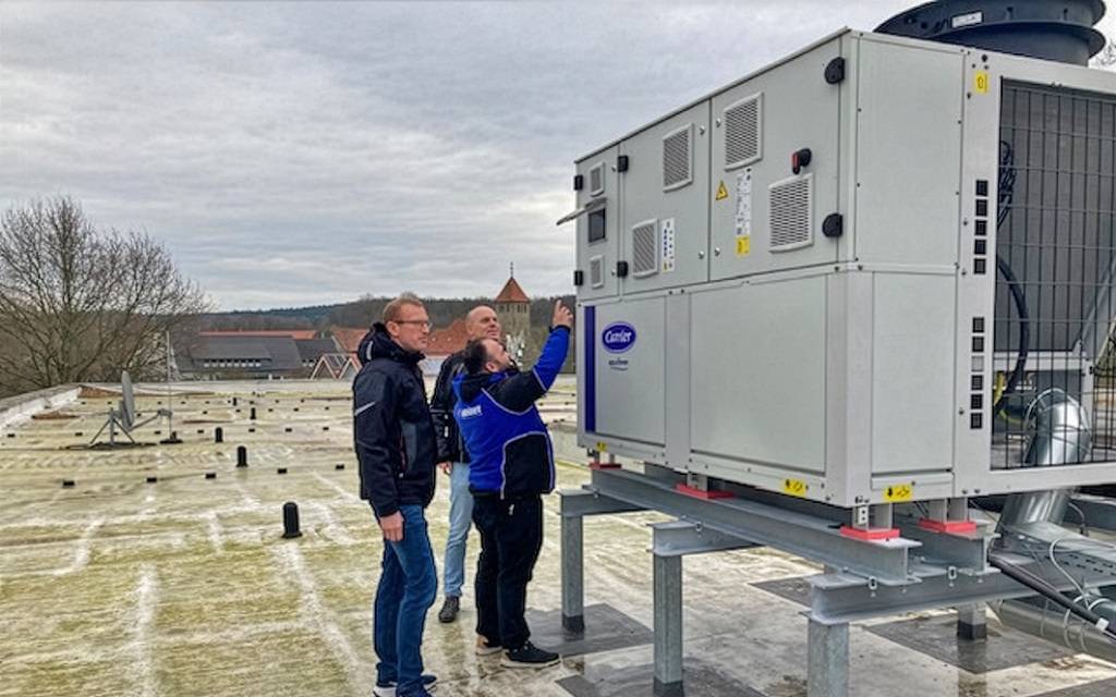 Drei Männer auf einem Flachdach an einer großen Wärmepumpe