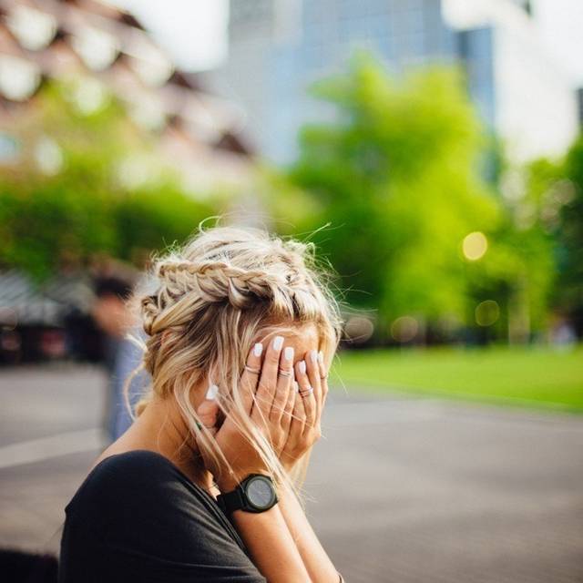 Blonde Frau vergräbt ihr Gesicht in den Händen.