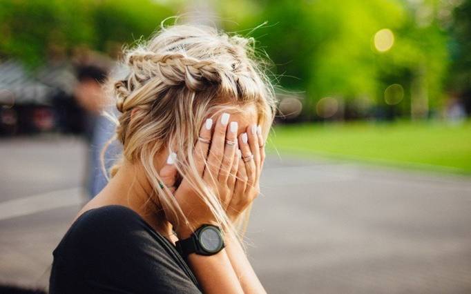 Blonde Frau vergräbt ihr Gesicht in den Händen.