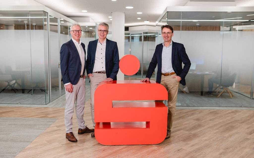 Der dreiköpfige Vorstand der Kreissparkasse Steinfurt hinter einem großen roten 3D-Sparkassenlogo