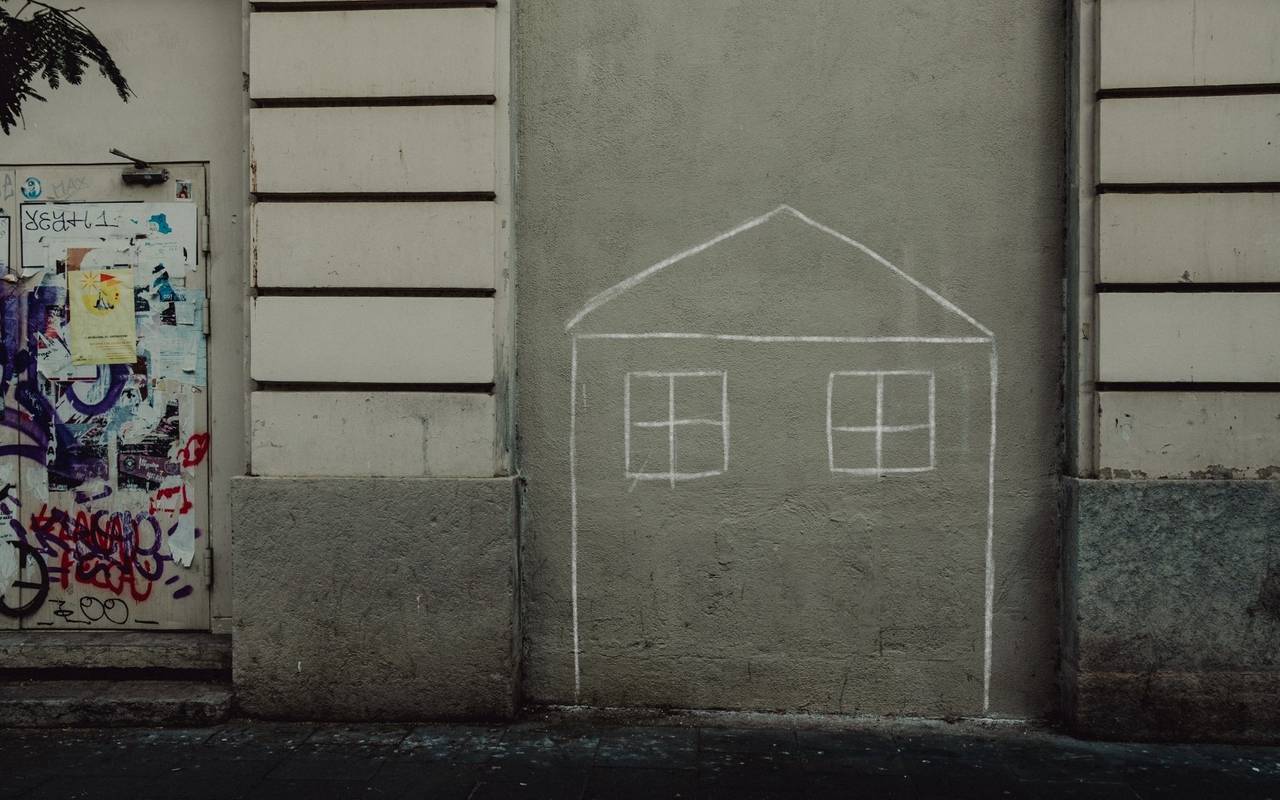 Auf einer Hauswand hat jemand mit Kreide ein Haus gezeichnet.