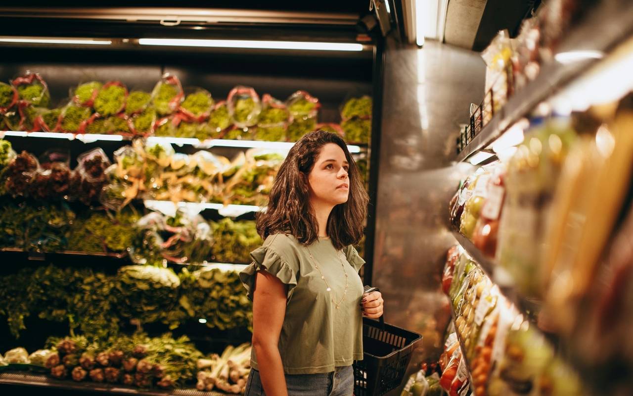 Eine Frau steht im Supermarkt und schaut in ein Regal.