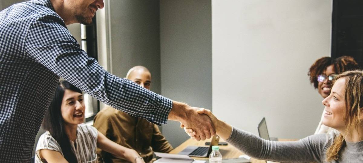 Junge Menschen interagieren freundlich rund um einen Tisch, teils sitzend, teils stehend.