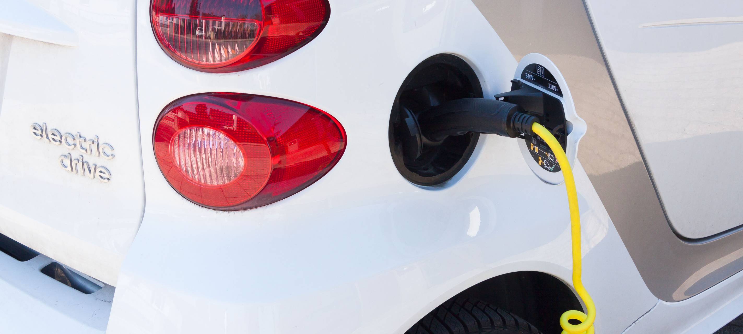Detailbild eines weißen Autohecks mit eingestecktem E-Ladekabel