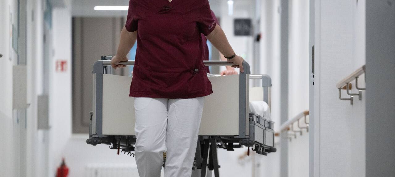 In einem Krankenhaus schiebt eine Krankenschwester ein Bett vor sich her.