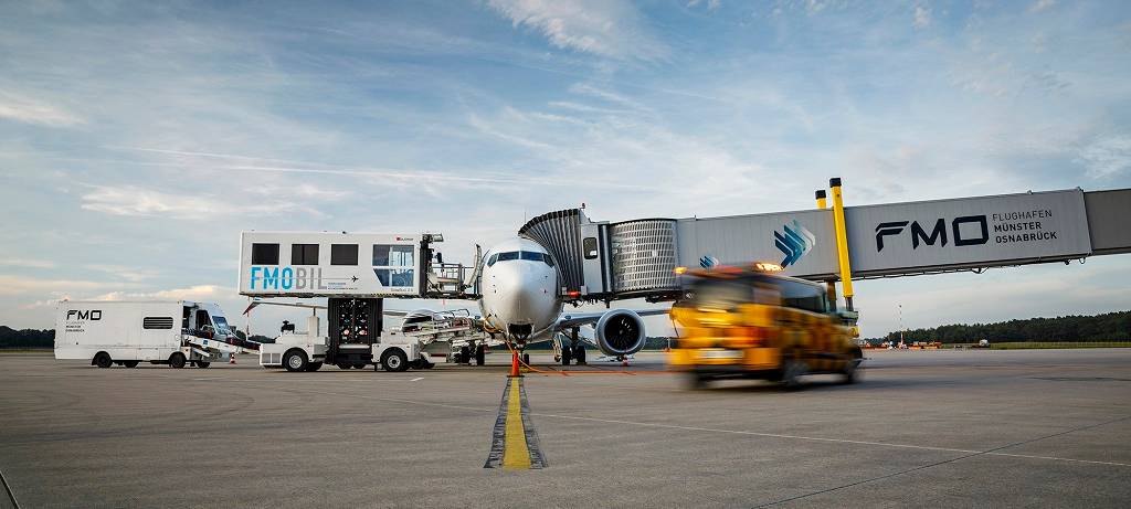 Auf dem Rollfeld steht ein Flugzeug. Es wird für den Abflug vorbereitet. Ein orange-farbenes Auto rollt an das Flugzeug heran.