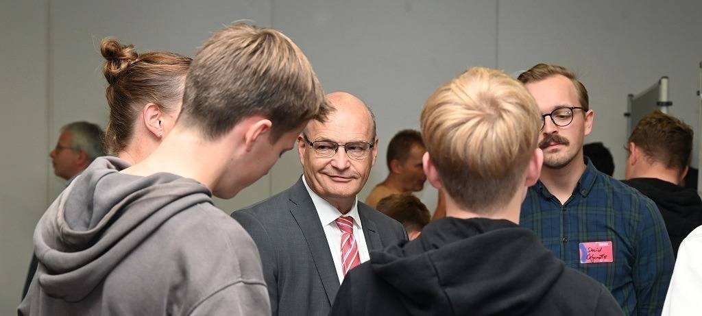 Menschengruppe im Gespräch: Zwei Jugendliche von hinten. Im Zentrum lächelt der Landrat.