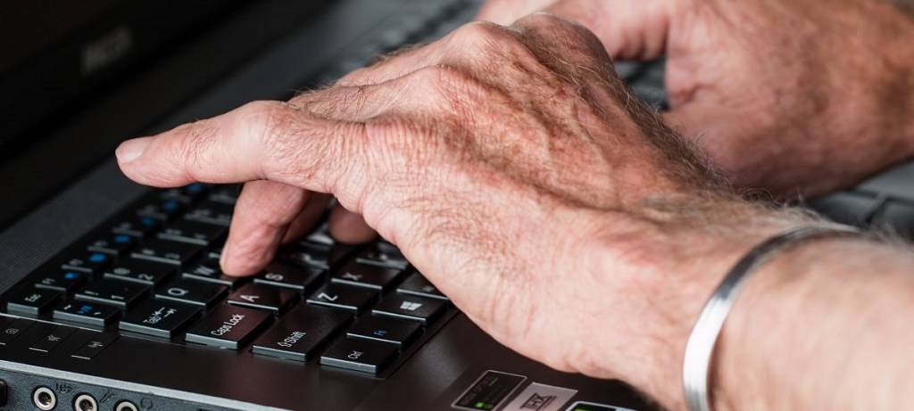 Männer-Hände, die auf einer Tastatur tippen. Links ein silberner Armreif.