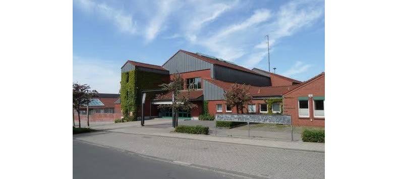 Der Eingang des Schulgebäudes. Ein roter Backsteinbau mit Zinkgiebeln und teilweisem Efeubewuchs.