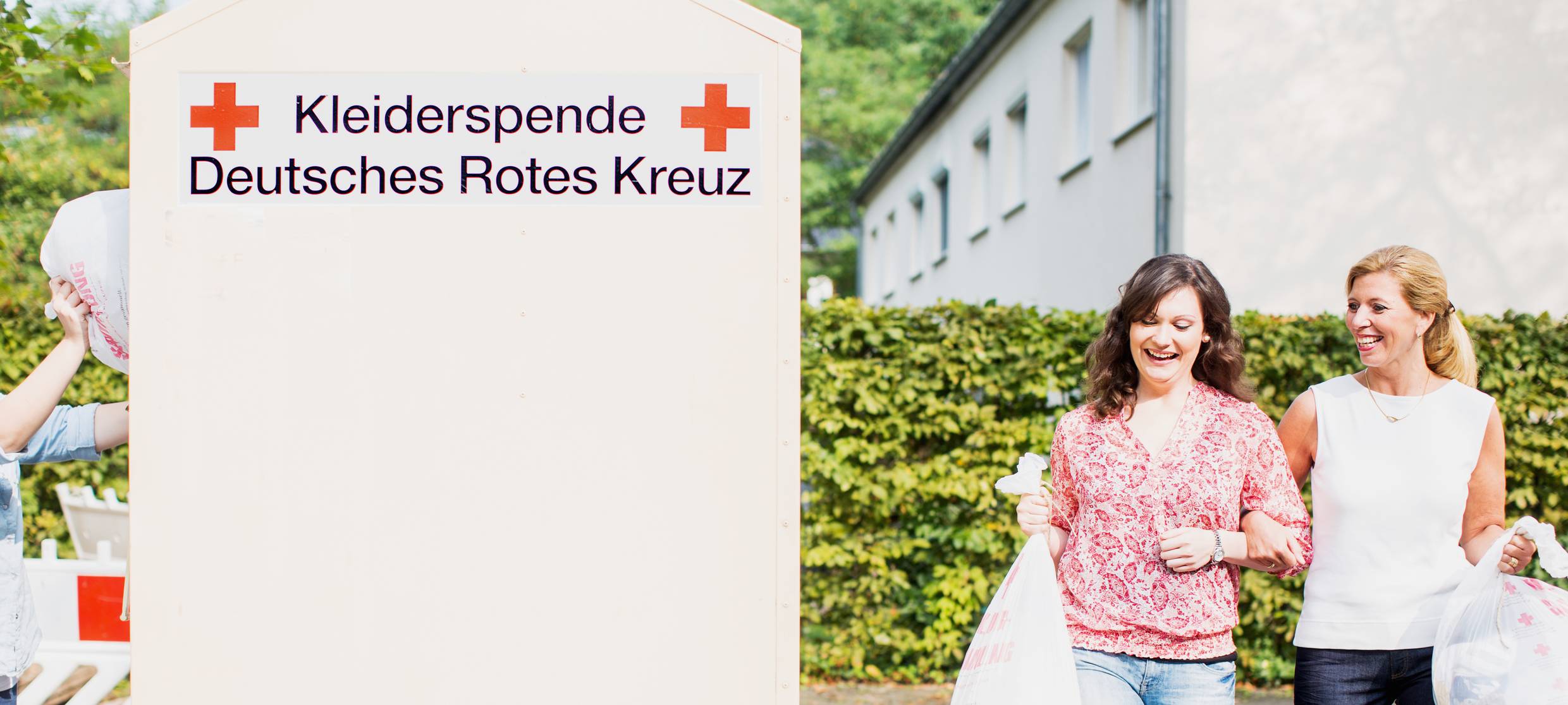Zwei Frauen gehen zu einem Altkleidercontainer des Deutschen Roten Kreuzes