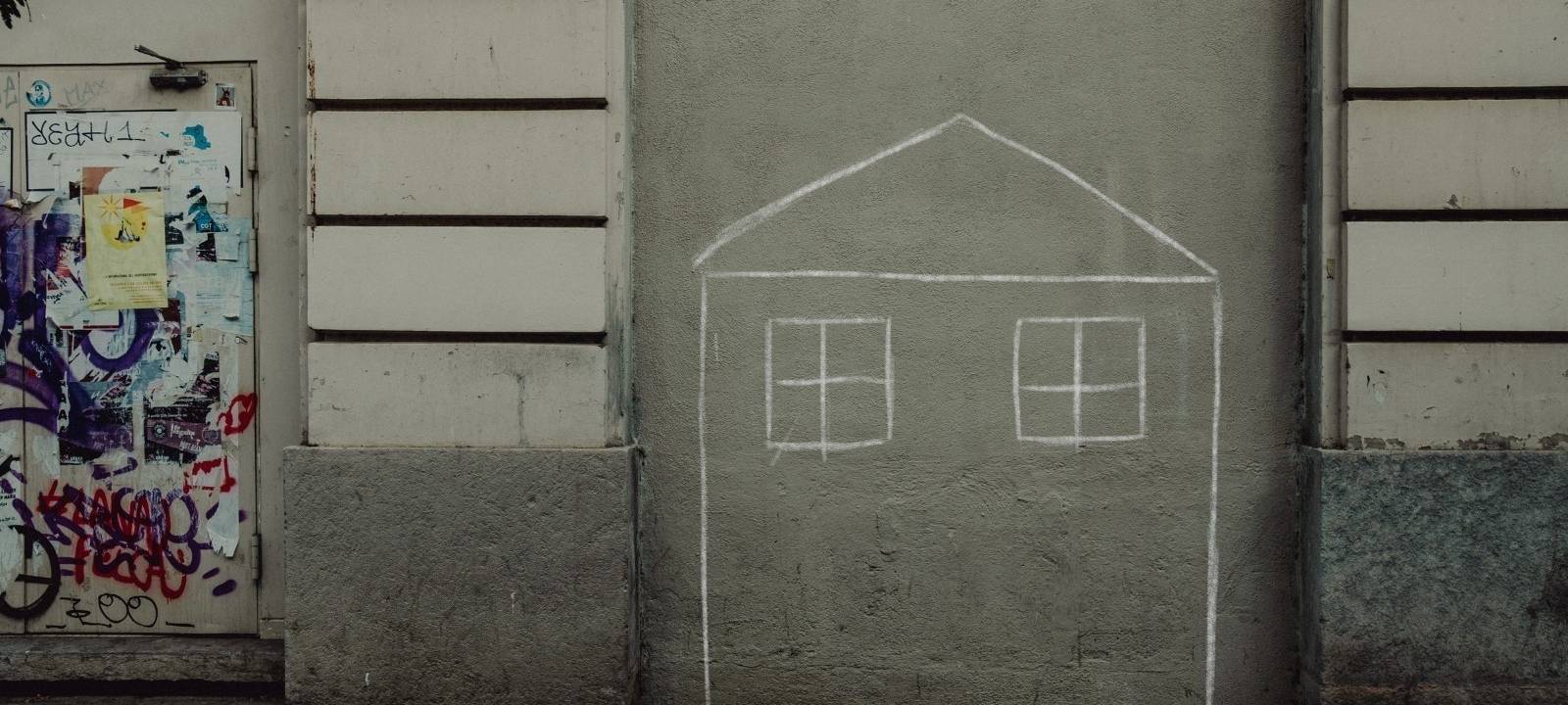 Auf einer Hauswand hat jemand mit Kreide ein Haus gezeichnet.