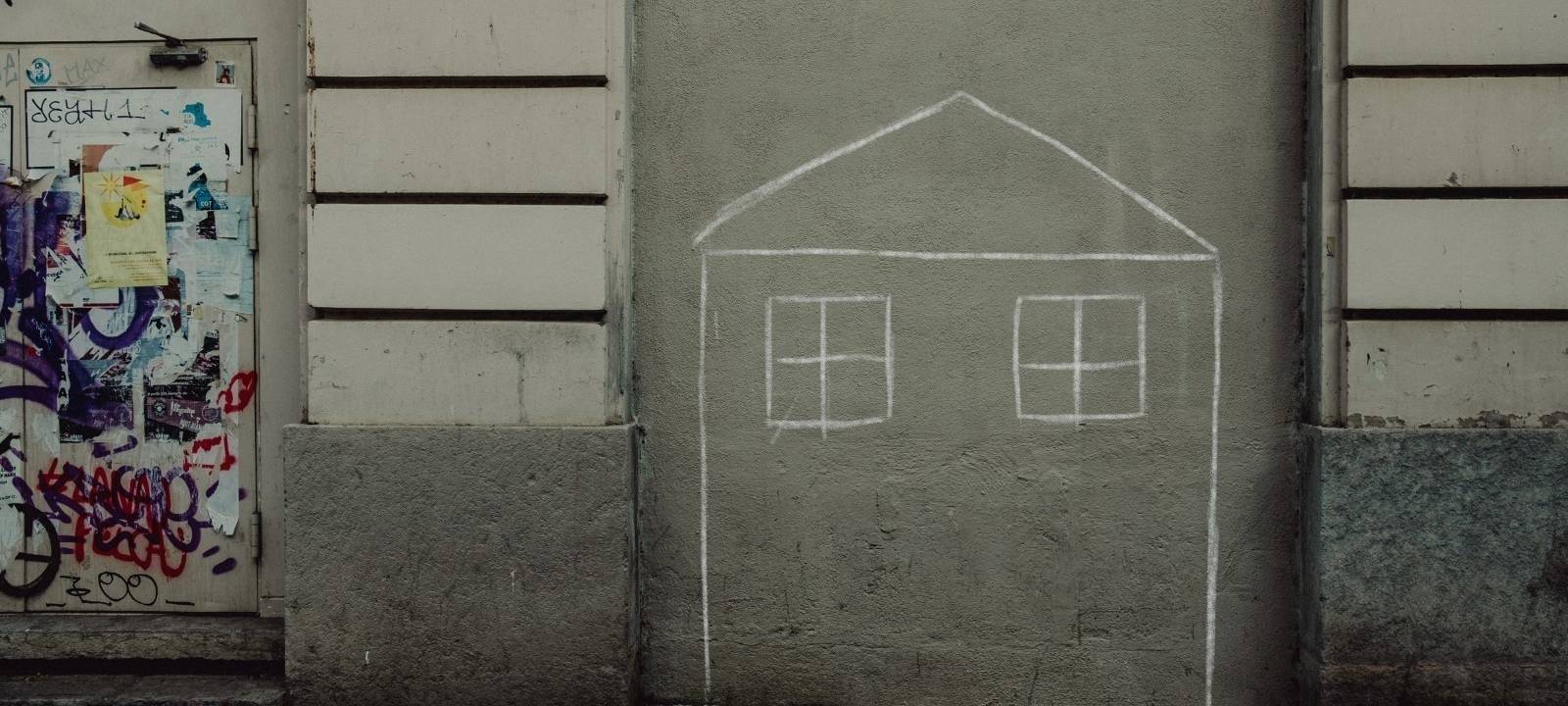 Auf einer Hauswand hat jemand mit Kreide ein Haus gezeichnet.