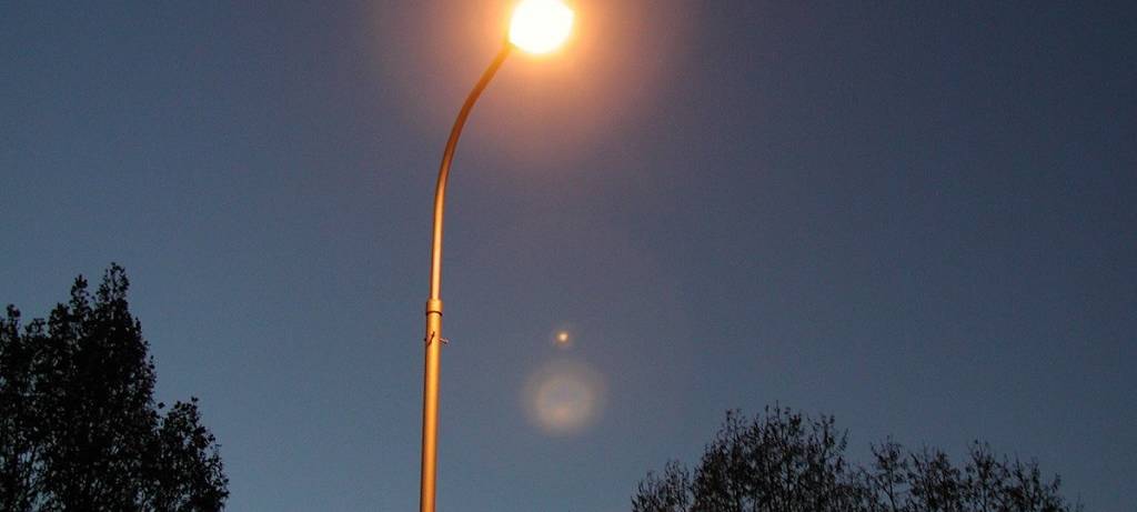 Straßenlampe vor klarem Nachthimmel. Im Hintergrund zwei Baumkronen.