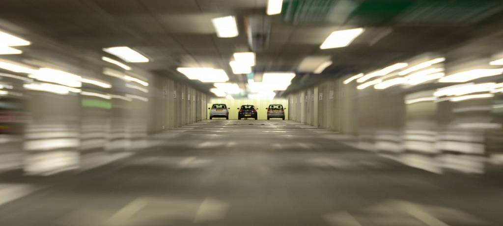 Ein verschwommener Blick in ein beleuchtetes Parkhaus. Am Ende der Hauptspur drei Autos von hinten, scharf aber weit weg.