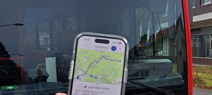 Im Hintergrund ein RVM-Bus, im Vordergrund eine Hand, die ein Handy hält. Darauf zu sehen: Die neue Busverbindung in der App.