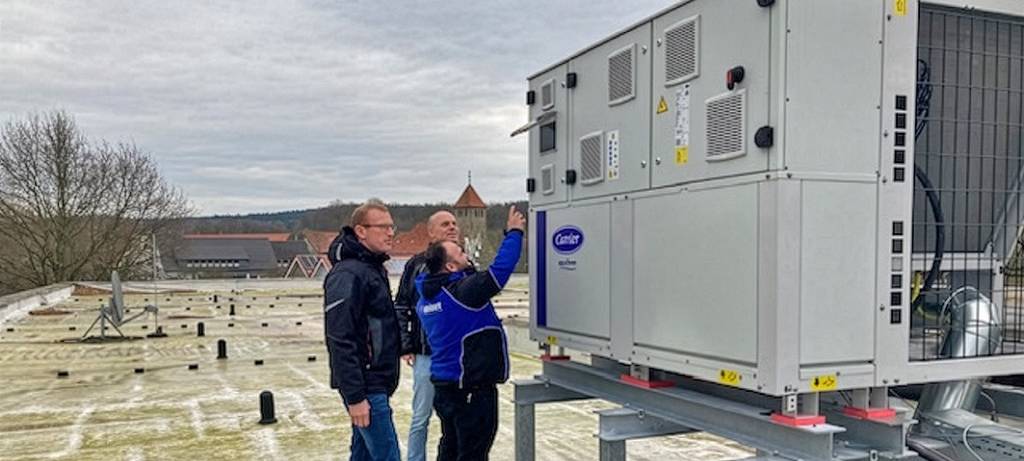 Drei Männer auf einem Flachdach an einer großen Wärmepumpe