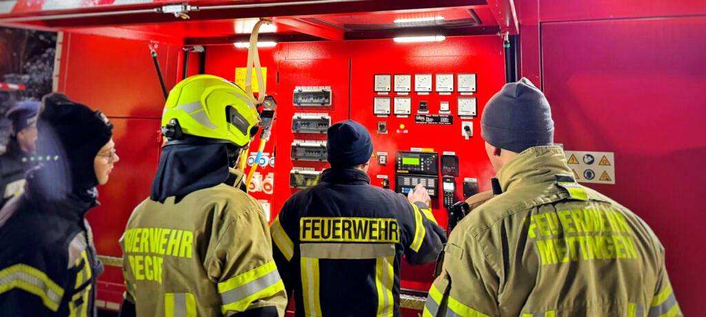 Feuerwehrleute (von hinten) an der Steuereinheit eines großen Notstromaggregats
