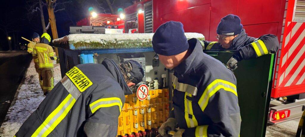 Feuerwehrleute in Einsatzkleidung schließen in der Nacht einen Stromkasten der öffentlichen Versorgung an ein Notstromaggregat an