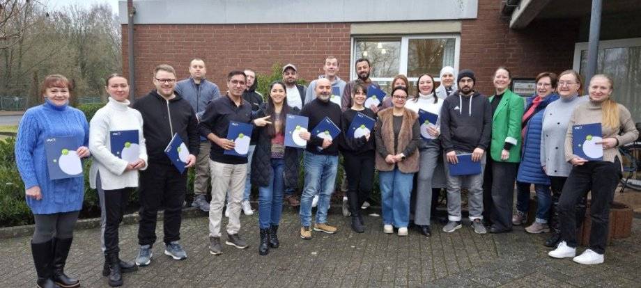 Menschen mit stolzem Lächeln und Abschlusszertifikaten vor einem Gebäude