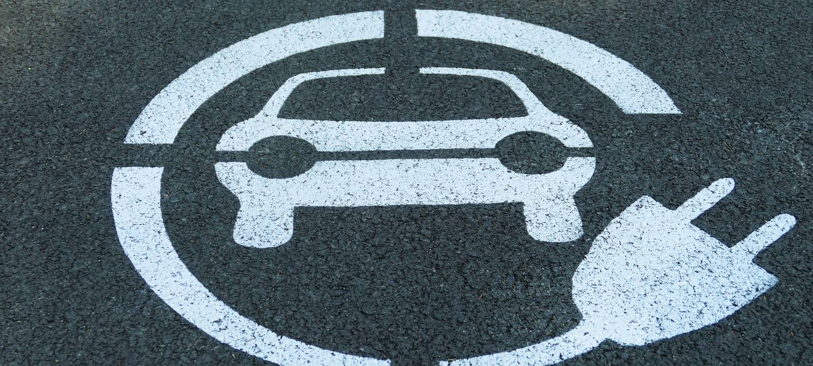 Auf der Straße ist ein Symbol gesprüht: ein Auto mit einem Stecker. Es ist ein Symbol für E-Autos.