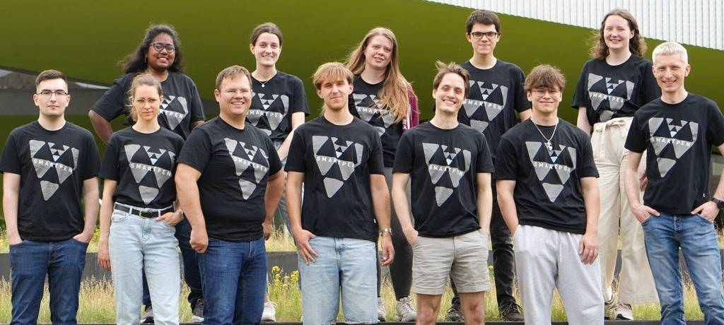 Zwölf junge Leute draußen vor einem Gebäude in T-Shirts mit der Aufschrift SMARTPEN