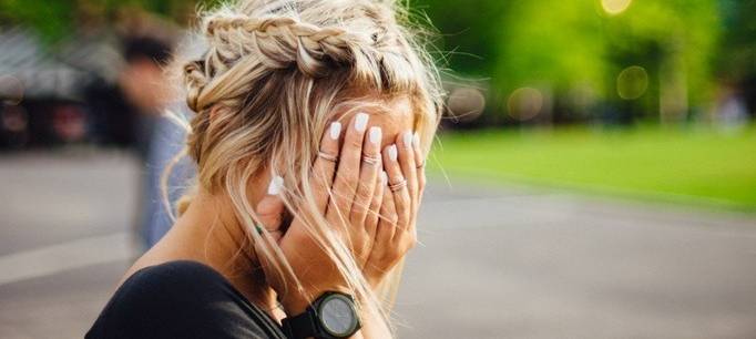 Blonde Frau vergräbt ihr Gesicht in den Händen.