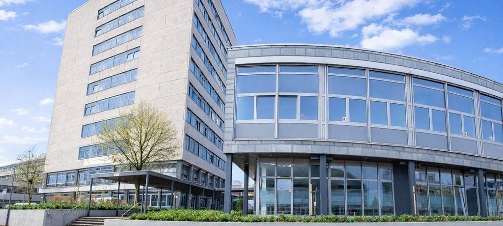 Ansicht der Kaufmännischen Schulen in Ibbenbüren: ein graues Gebäude mit viel Glasflächen. Ein Teil der Fassade ist gebogen.