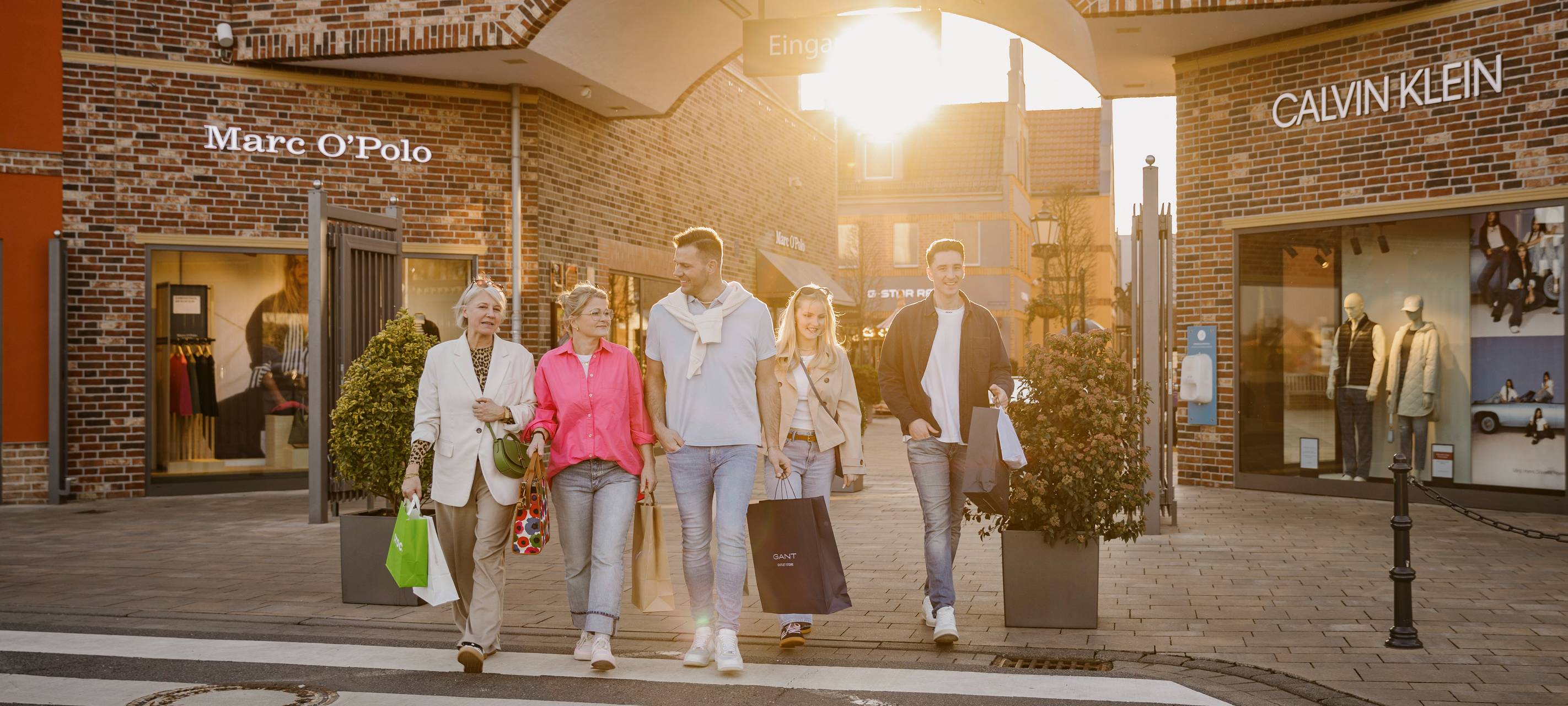 Glückliche Menschen laufen aus dem Designer Outlet Ochtrup in Richtung des Parkplatzes.