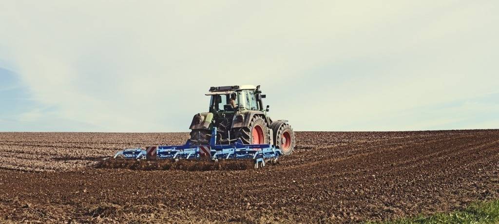 Auf einem Feld fährt eine landwirtschaftliche Maschine bei der Arbeit durch die Anbaufläche. Das Bild steht sinnbildlich für die wirtschaftlichen Herausforderungen vieler Höfe.