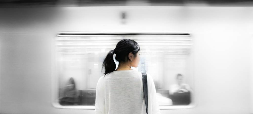 Frau an einem Bahnsteig, während im Hintergrund ein Zug durchfährt
