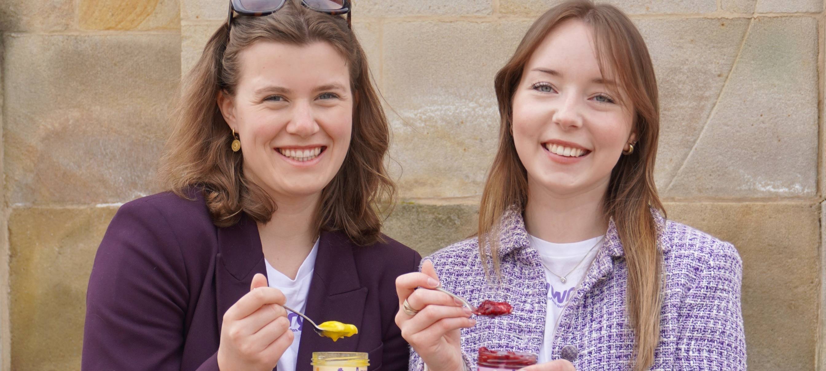 Zwei junge Frauen sitzen auf einer Treppe und präsentieren das Produkt rawry: Veganer, roher Kuchen im Glas.