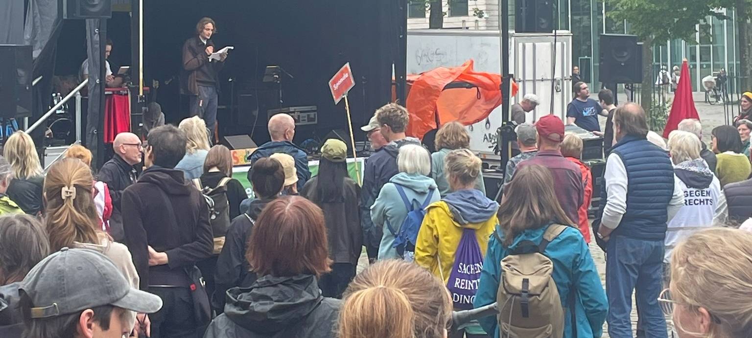 Demonstranten stehen vor einer Bühne in Münster.
