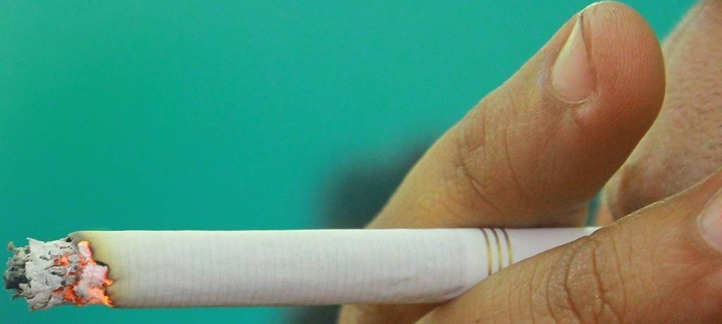 Detailaufnahme Rauchen: Zigarette zwischen Zeige- und Mittelfinger und im Mund